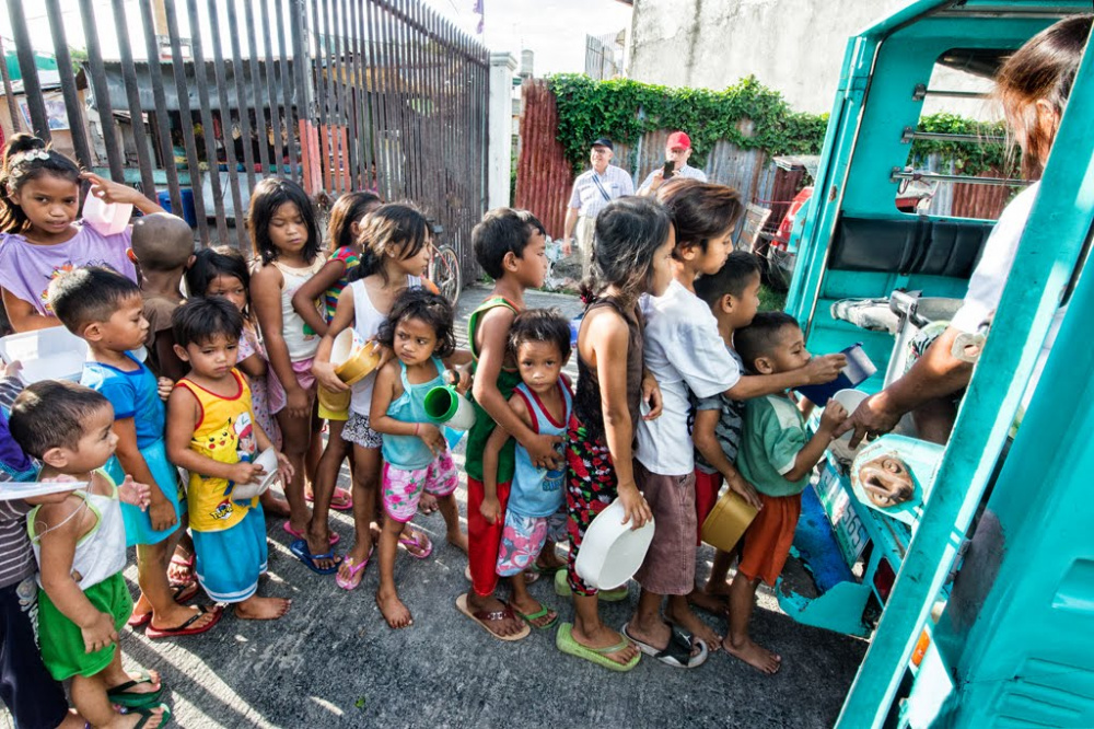 fila di bambini lungo strada davanti ad una baraccopoli per la distribuzione del cibo